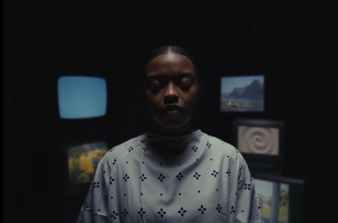 Still — subject under simulation, eyes closed, surrounded by monitors